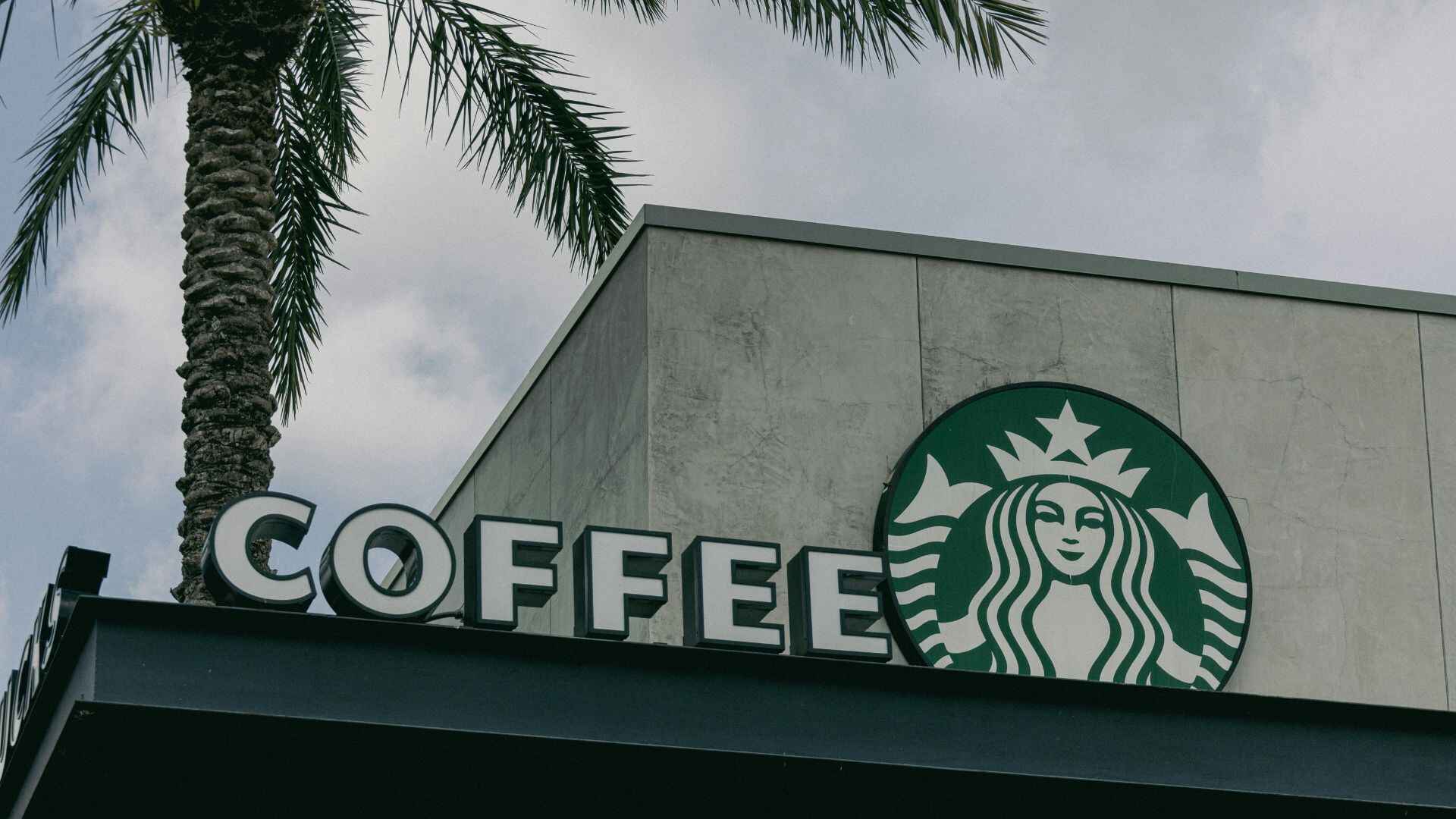 Exterior of a Starbucks store with logo and “Coffee” sign under a palm tree, illustrating strong brand presence
